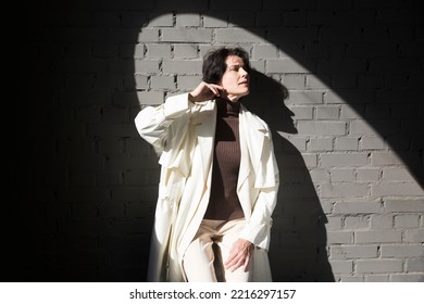 Middle Aged Woman  In A White Cloak Relaxing Against A Gray Wall. Copy Space. 