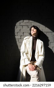 Middle Aged Woman  In A White Cloak Relaxing Against A Gray Wall. Copy Space. 