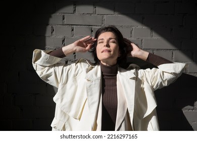 Middle Aged Woman  In A White Cloak Relaxing Against A Gray Wall. Copy Space. 