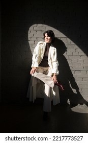 Middle Aged Woman  In A White Cloak Relaxing Against A Gray Wall. Copy Space. 