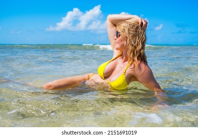 Middle aged woman in yellow bikini swimming on tropical beach