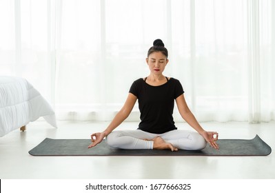 Middle aged women practicing yoga in Easy seat pose or Sukhasana with with mudra. Meditation with yoga in white bedroom after wake up in the morning. Concept of exercise, relaxation and healthcare.