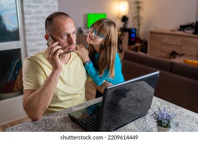 Middle Aged Working Father Talking On The Phone While Babysitting His Playful Daughter At Home. Cheerful Playful Kid Sitting On Neck Of Unhappy Busy Dad. Multi-tasking, Freelance, Fatherhood 