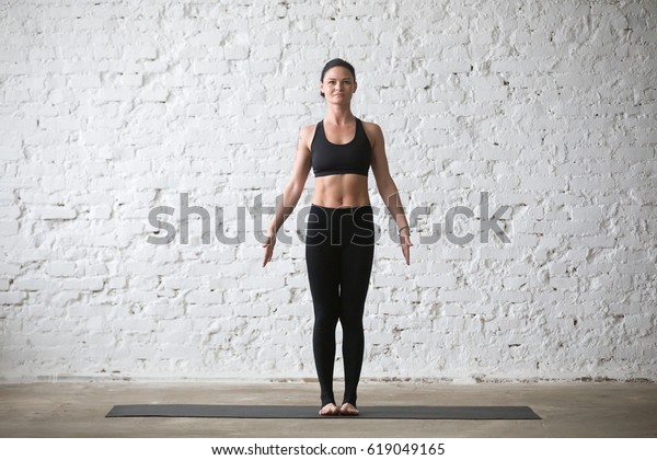 Middle aged yogi attractive smiling woman\
practicing yoga concept, standing in mountain exercise, Tadasana\
pose, working out, wearing black sportswear top and pants, full\
length, white loft\
background
