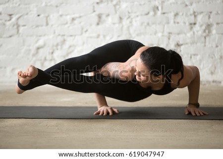 Middle aged yogi attractive woman practicing yoga concept, standing in Astavakrasana exercise, Eight Angle pose, working out wearing black sportswear pants, full length, white loft background 