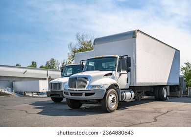 Middle duty Industrial standard white day cab rig semi trucks with box trailers for local deliveries and small business needs standing on the warehouse parking lot waiting for the next load - Powered by Shutterstock