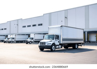 Middle duty Industrial standard white day cab rig semi trucks with box trailers for local deliveries and small business needs standing on the warehouse parking lot waiting for the next load - Powered by Shutterstock