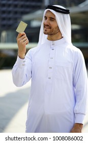 Middle East Business Man Showing His Business Card. Cropped Image Of Handsome Guy Holding A Credit Card And Smiling.Young Man Holding Smart Card In Hand. The Man Looking To The Chip Card Outdoor.