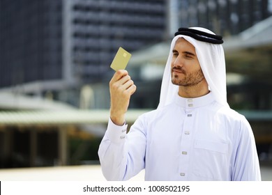 Middle East Business Man Showing His Business Card. Cropped Image Of Handsome Guy Holding A Credit Card And Smiling.Young Man Holding Smart Card In Hand. The Man Looking To The Chip Card Outdoor.