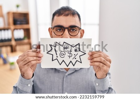 Middle east man with beard holding banner with swear words relaxed with serious expression on face. simple and natural looking at the camera. 