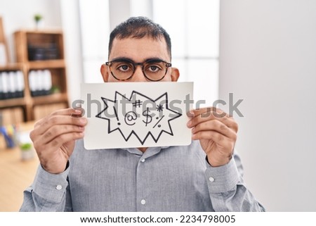 Middle east man with beard holding banner with swear words in shock face, looking skeptical and sarcastic, surprised with open mouth 