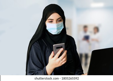 Middle Eastern Arab Woman At A Hospital Reception Wearing Protective Face Mask And Traditional Hijab Abaya. Emirati Girl Works At A Healthcare Company