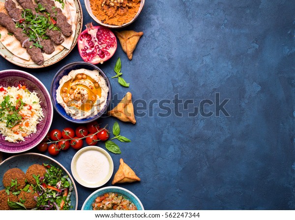 Middle eastern or arabic dishes and assorted meze on\
concrete rustic background. Meat kebab, falafel, baba ghanoush,\
hummus, sambusak, rice, tahini, kibbeh, pita. Halal food. Space for\
text. Top view