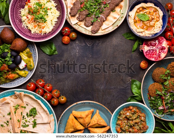 Middle eastern or arabic dishes and assorted meze on\
a dark background. Meat kebab, falafel, baba ghanoush, hummus, rice\
with vegetables, sambusak, kibbeh, pita. Halal food. Space for\
text. Top view