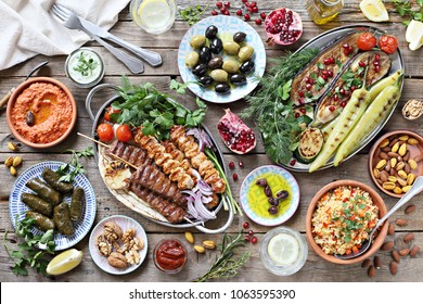 Middle Eastern, Arabic Or Mediterranean Dinner Table With Grilled Lamb Kebab, Chicken Skewers  With Roasted Vegetables And Appetizers Variety Serving On Wooden Outdoor Table. Overhead View.