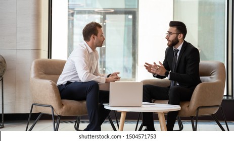 Middle eastern and caucasian ethnicity businessmen seated on armchair in modern office talking solve common issues, banker telling to client regarding bank services make recommendations and consulting