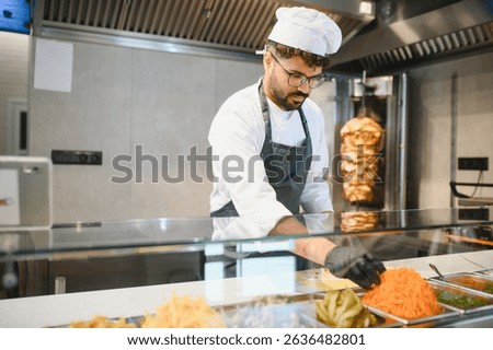 Middle eastern chef adding grated carrots to other fresh ingredients while preparing a doner kebab or shawarma in a fast food restaurant