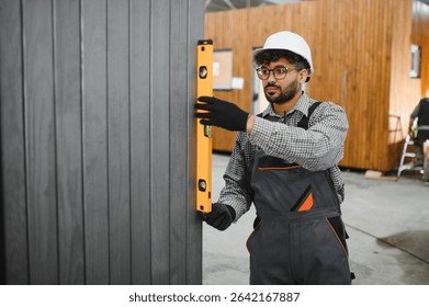 Middle eastern construction worker using a spirit level while installing a prefabricated wall panel in a modular house factory