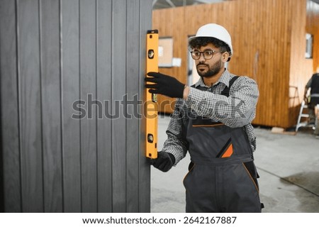 Middle eastern construction worker using a spirit level while installing a prefabricated wall panel in a modular house factory