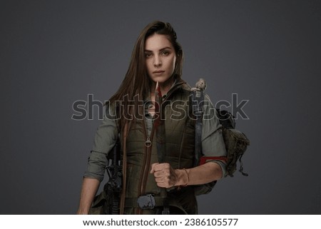 Middle Eastern descent in post-apocalyptic survival gear, brandishing a dagger on a gray backdrop, showcasing her determination to survive