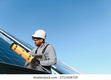 Middle eastern engineer uses a level tool while installing a solar panel on a clear day, promoting renewable energy and sustainable practices