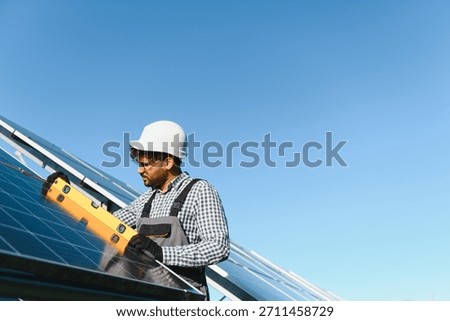 Middle eastern engineer uses a level tool while installing a solar panel on a clear day, promoting renewable energy and sustainable practices