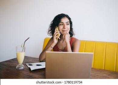 Middle Eastern freelancer using smartphone application for calling to colleague and discuss startup project details, successful woman with laptop and planner notepad phoning for talking via cellphone