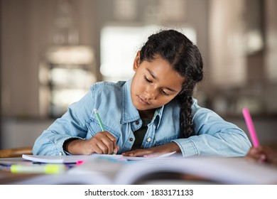 Middle eastern girl doing homework writing and reading at home. Concentrated beautiful indian female child writing in her notebook. Focused latin schoolgirl studying and preparing for exams.
