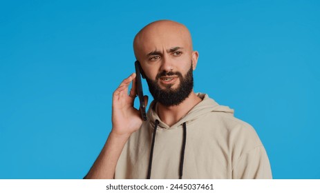 Middle eastern guy chatting with friends on phone call, answering smartphone while standing over blue background. Modern man discussing something on a remote network. Camera 2. Handheld shot. - Powered by Shutterstock