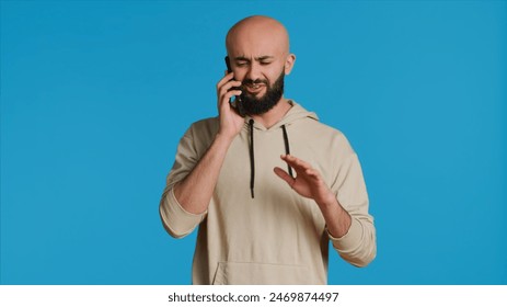 Middle eastern guy chatting with friends on phone call, answering smartphone while standing over blue background. Modern man discussing something on a remote network. Camera 1. - Powered by Shutterstock