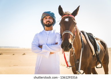 Middle Eastern Handsome Man With Typical Emirates Dress Riding A Arabic Horse In The Dubai Desert