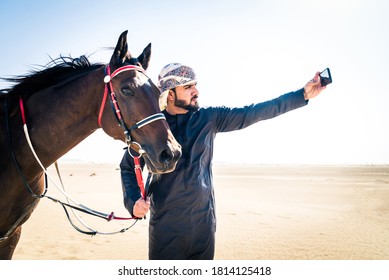 Middle Eastern Handsome Man With Typical Emirates Dress Riding A Arabic Horse In The Dubai Desert