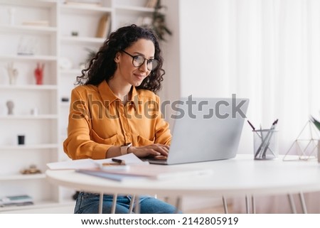 Middle Eastern Lady Using Laptop Working Online Wearing Eyewear Sitting At Workplace In Modern Office. Remote Job, Technology And Career Profession Concept. Side View