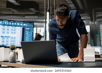 Middle eastern male developer studying land regulations on laptop in the office, working on redevelopment for a residential construction project in an urban innovation hub. Construction site.