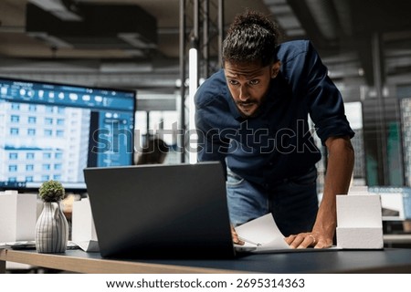 Middle eastern male developer studying land regulations on laptop in the office, working on redevelopment for a residential construction project in an urban innovation hub. Construction site.