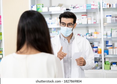 Middle Eastern Male Pharmacist Wearing Protective Hygienic Mask To Prevent Infection Selling Medications To Woman Patient To Prescription And Making Drug Recommendations In Modern Pharmacy