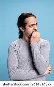 Middle eastern man biting his nails due to stress and anxiety in studio, having a nervous tic and being worried about something. Young adult under pressure feeling concerned, fear and distress.
