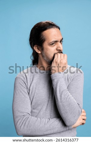 Middle eastern man biting his nails due to stress and anxiety in studio, having a nervous tic and being worried about something. Young adult under pressure feeling concerned, fear and distress.