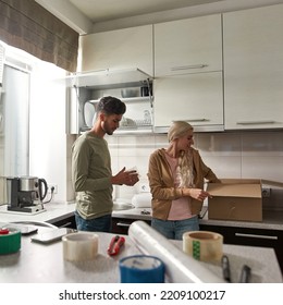 Middle Eastern Man Packing Glass In Air Bubble Film While European Girl Putting Something In Cardboard Box. Young Multiethnic Couple Moving To New Apartment. Concept Of Home Relocation. Modern Kitchen