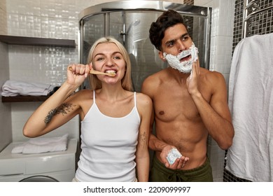 Middle Eastern Man Smearing Beard With Shaving Foam While European Girl Brushing Teeth With Toothbrush In Bathroom At Morning Time. Domestic Lifestyle. Face Skin Care. Young Focused Multiracial Couple