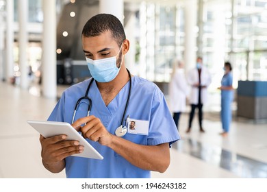 Middle eastern nurse using digital tablet while wearing surgical mask. Busy doctor working on digital tablet and wearing protective face mask for coronavirus safety. Healthcare indian worker in clinic - Powered by Shutterstock