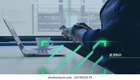 Middle Eastern professional checking smartwatch at office desk with laptop, mug and HUD, copy space. Technology, futuristic, modern, productivity, innovation, corporate, digital