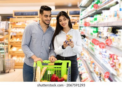 Middle Eastern Spouses Holding Dairy Products Doing Grocery Shopping Together In Modern Supermarket. Arab Family Buying Food In Store On Weekend. Consumerism And Household