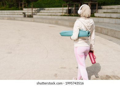 Middle eastern woman in hijab listening music with headphones while walking outdoors - Powered by Shutterstock