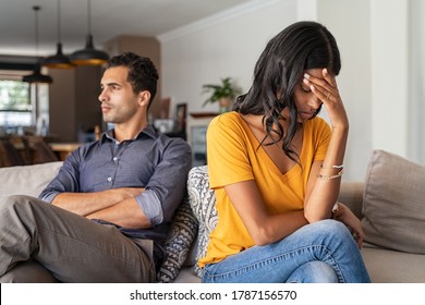 Middle eastern young couple sitting on couch after a fight. Sad indian woman sitting with hand on head after quarrel with boyfriend at home. Angry couple ignoring each other, relationship troubles.