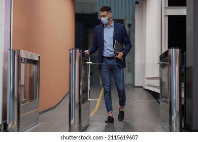 Middle eastern young man in protective face mask holding Electronic entrance gate card and laptop, worker passing access building security system at office, panorama with copy space, full length