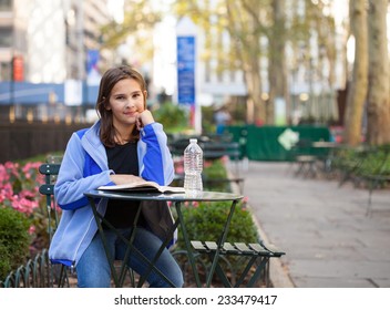 Middle School Girl Sitting In A City Park In New York Reading A Book With A Bottle Of Water