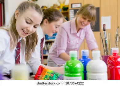 Middle School Student Painting In An Art Class With Her Art Teacher And Classmate In The Background.