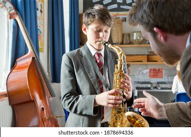 Middle School Student Playing A Saxophone In A Music Class With A Music Teacher Guiding Him.