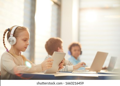 Middle School Students Sitting In Classroom Using Modern Headphones And Computers During Lesson, Horizontal Shot, Copy Space